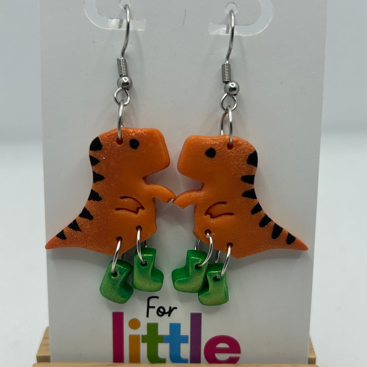 Dinosaur-shaped earrings with green gumboots on a display card.