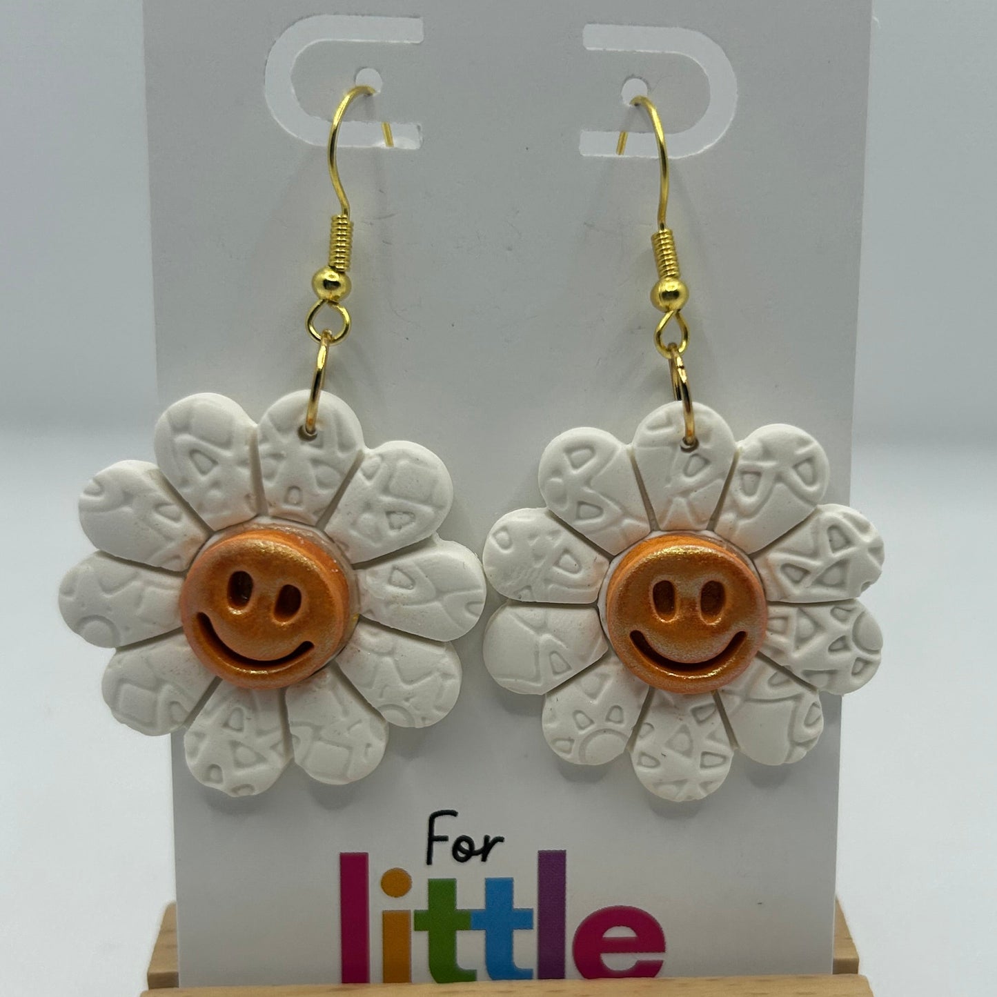 Flower-shaped earrings with smiley faces on a display card.