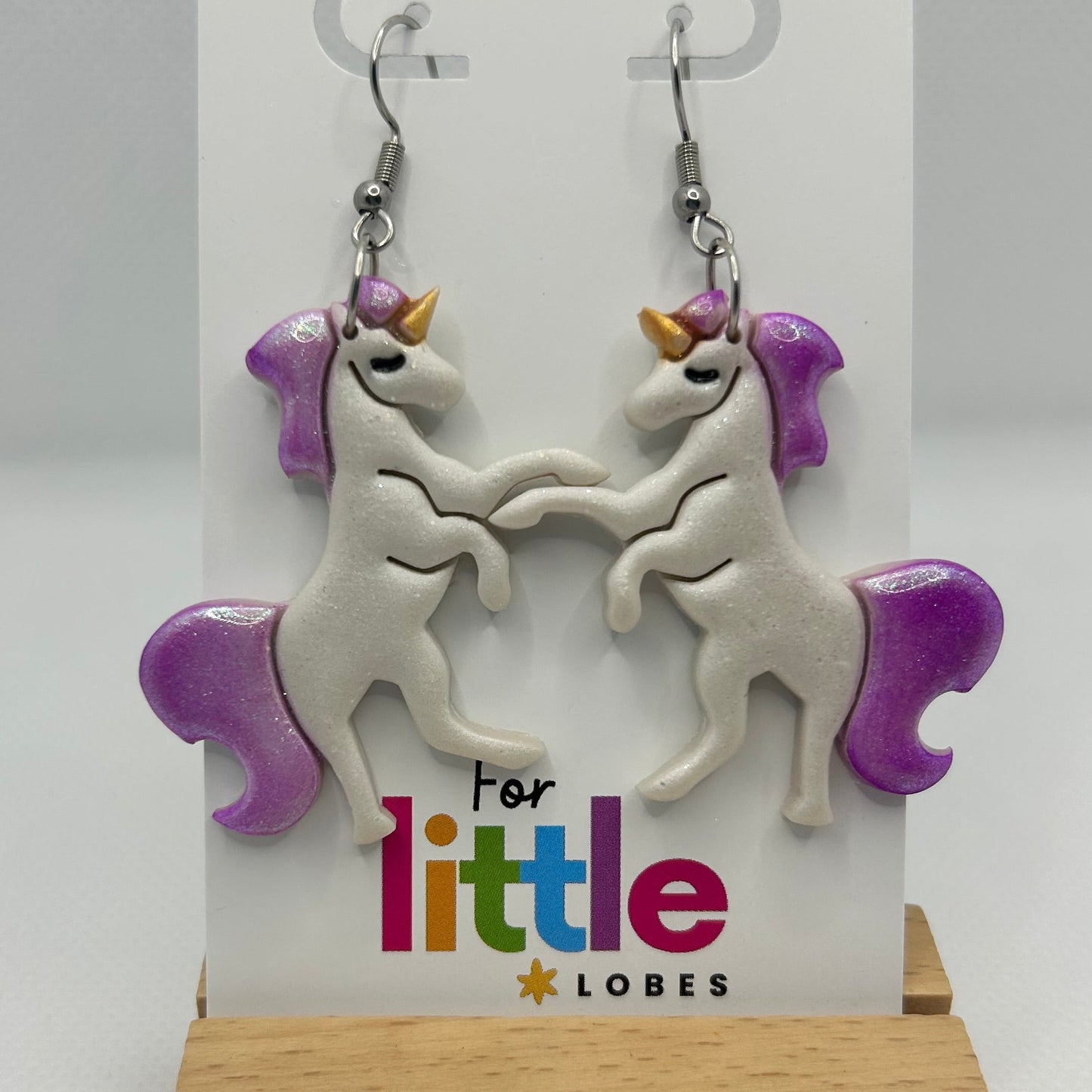 Unicorn-shaped earrings with purple manes and tails on a card with 'For little lobes' text