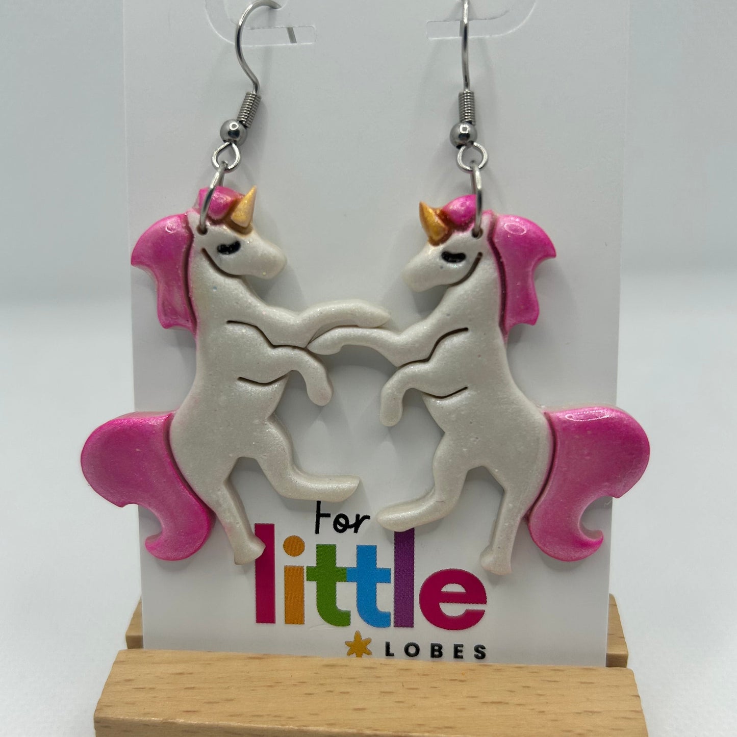 Unicorn-shaped earrings with pink manes and tails on a card with 'For little lobes' text