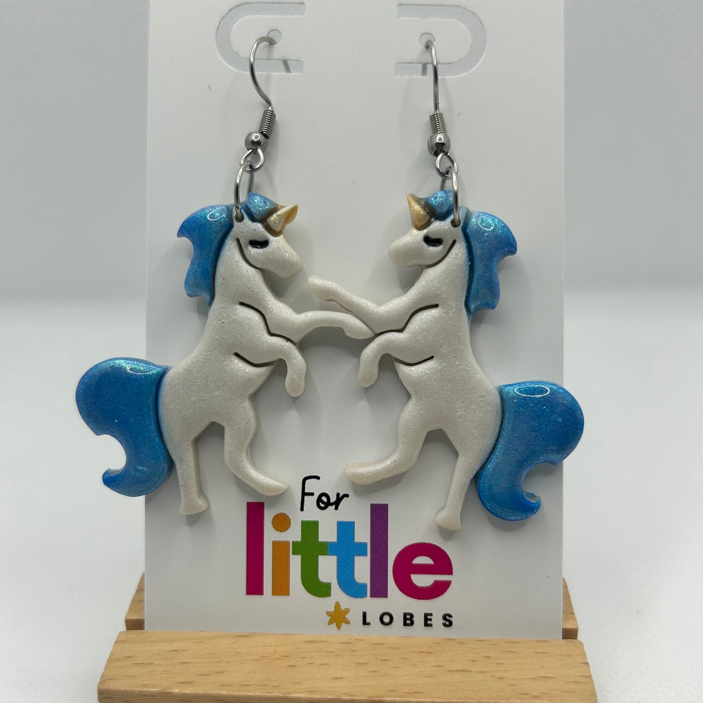 Unicorn-shaped earrings with blue manes and tails on a card with 'For little lobes' text