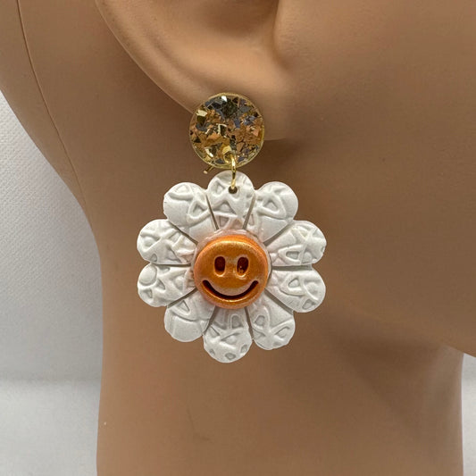 White flower-shaped earring with a smiley face on a mannequin ear.