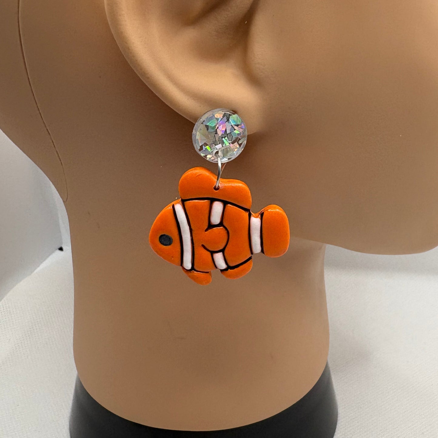 Orange, black and white clownfish earring hanging from the ear of a mannequin head.