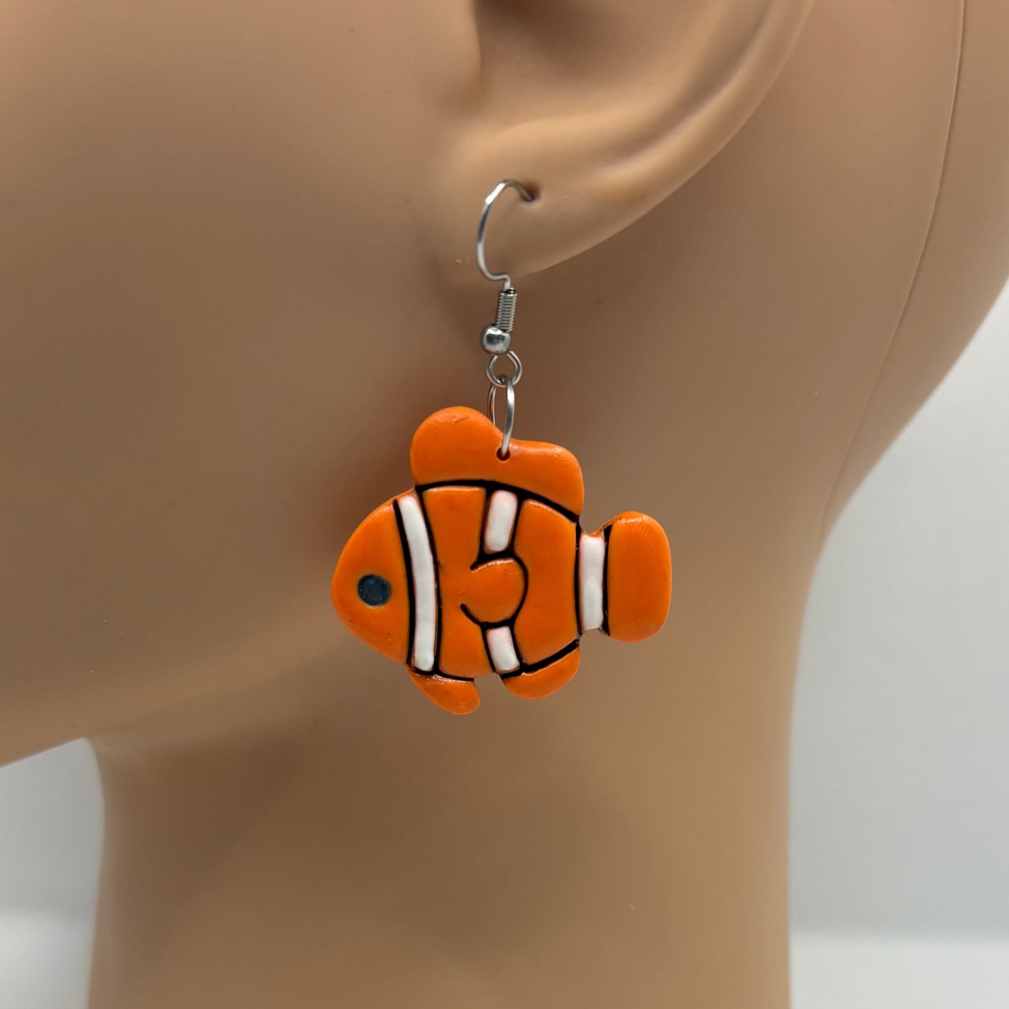 Orange, black and white clownfish earring hanging from the ear of a mannequin head.
