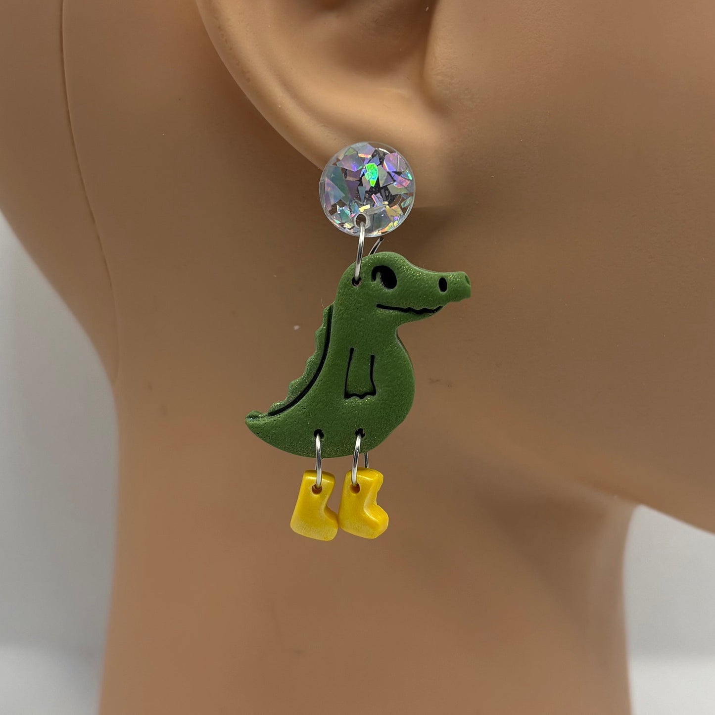 Green crocodile-shaped earrings with yellow gumboots on a mannequin head.