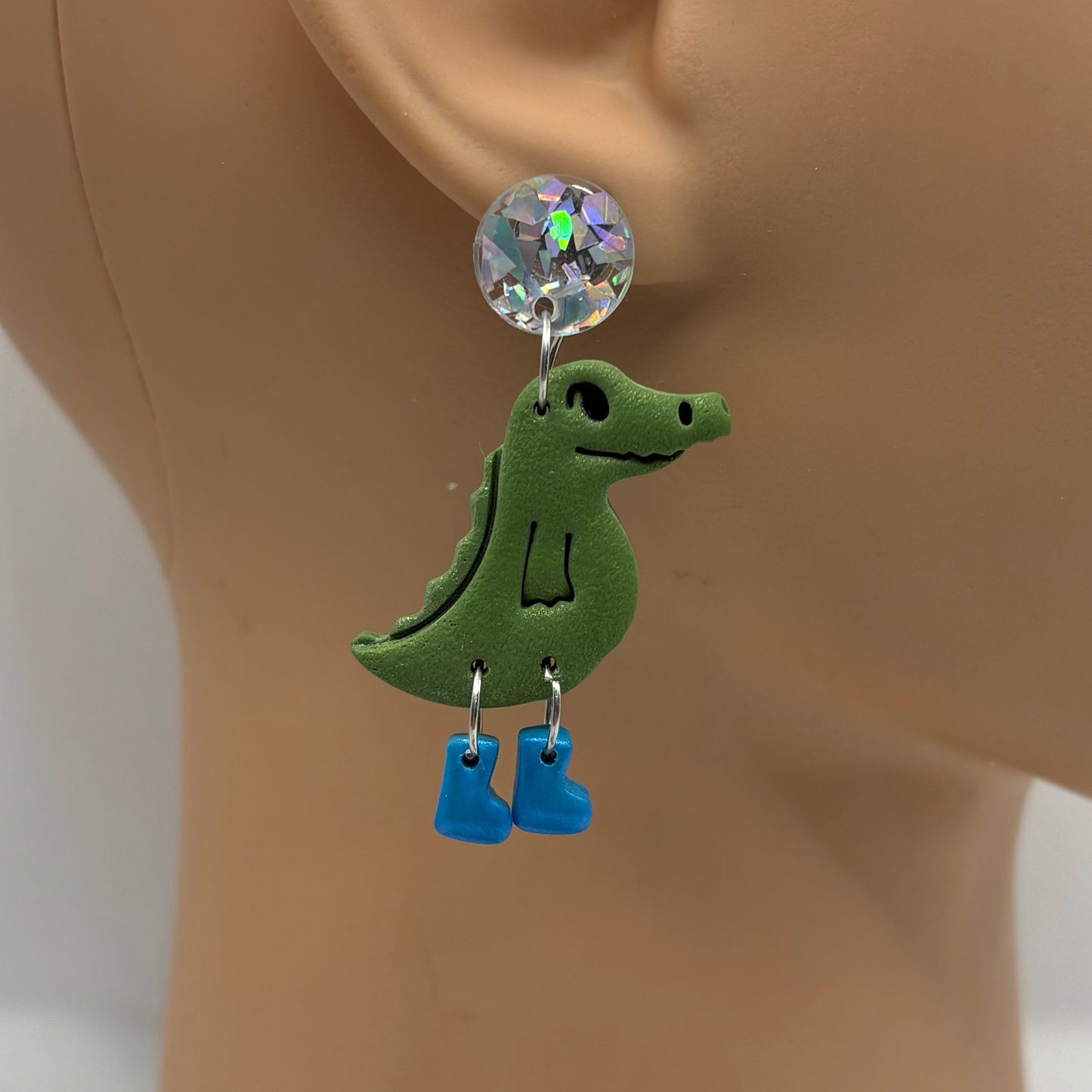 Green crocodile-shaped earrings with blue gumboots on a mannequin head.