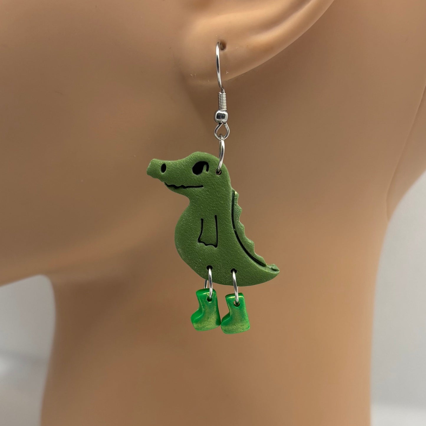 Green crocodile-shaped earrings with green gumboots on a mannequin head.