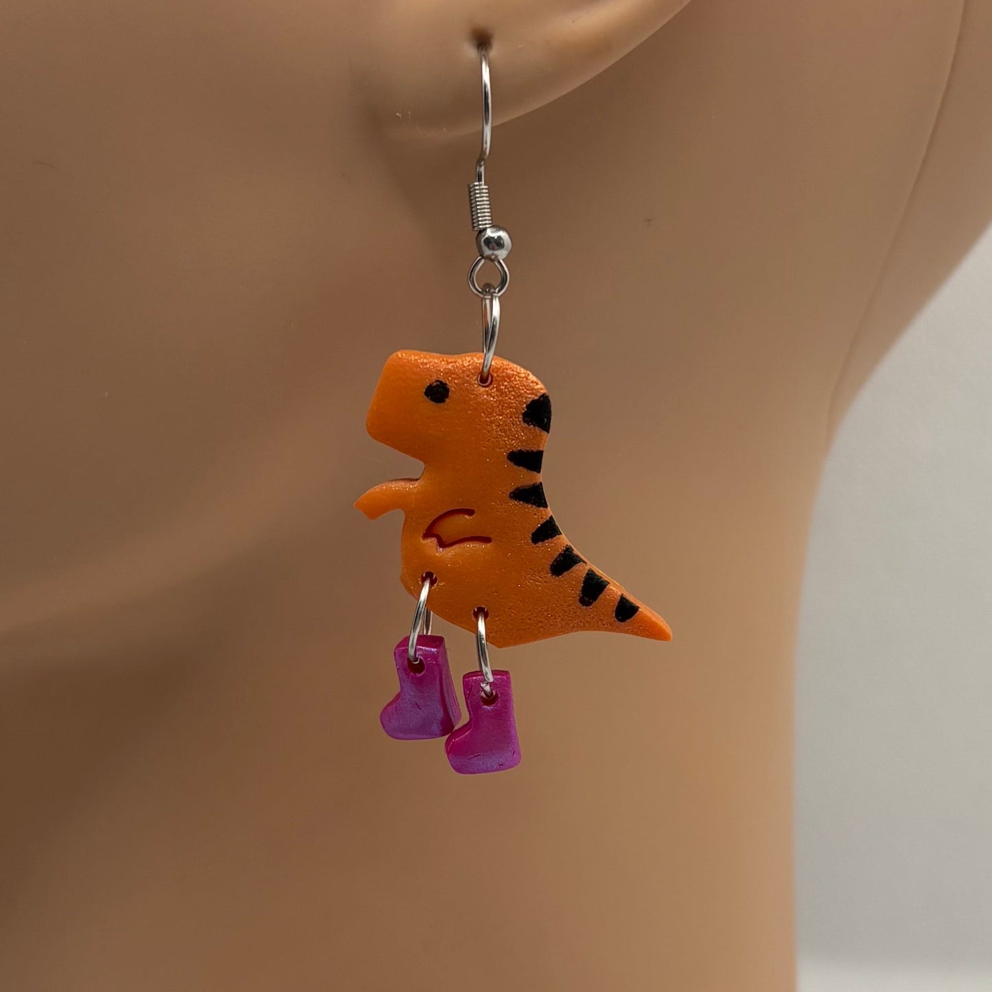 Dinosaur themed earrings with purple gumboots hanging from the ear of a mannequin head.