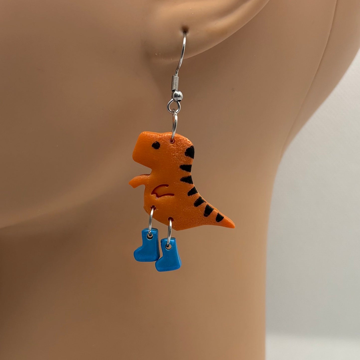 Dinosaur themed earrings with blue gumboots hanging from the ear of a mannequin head.