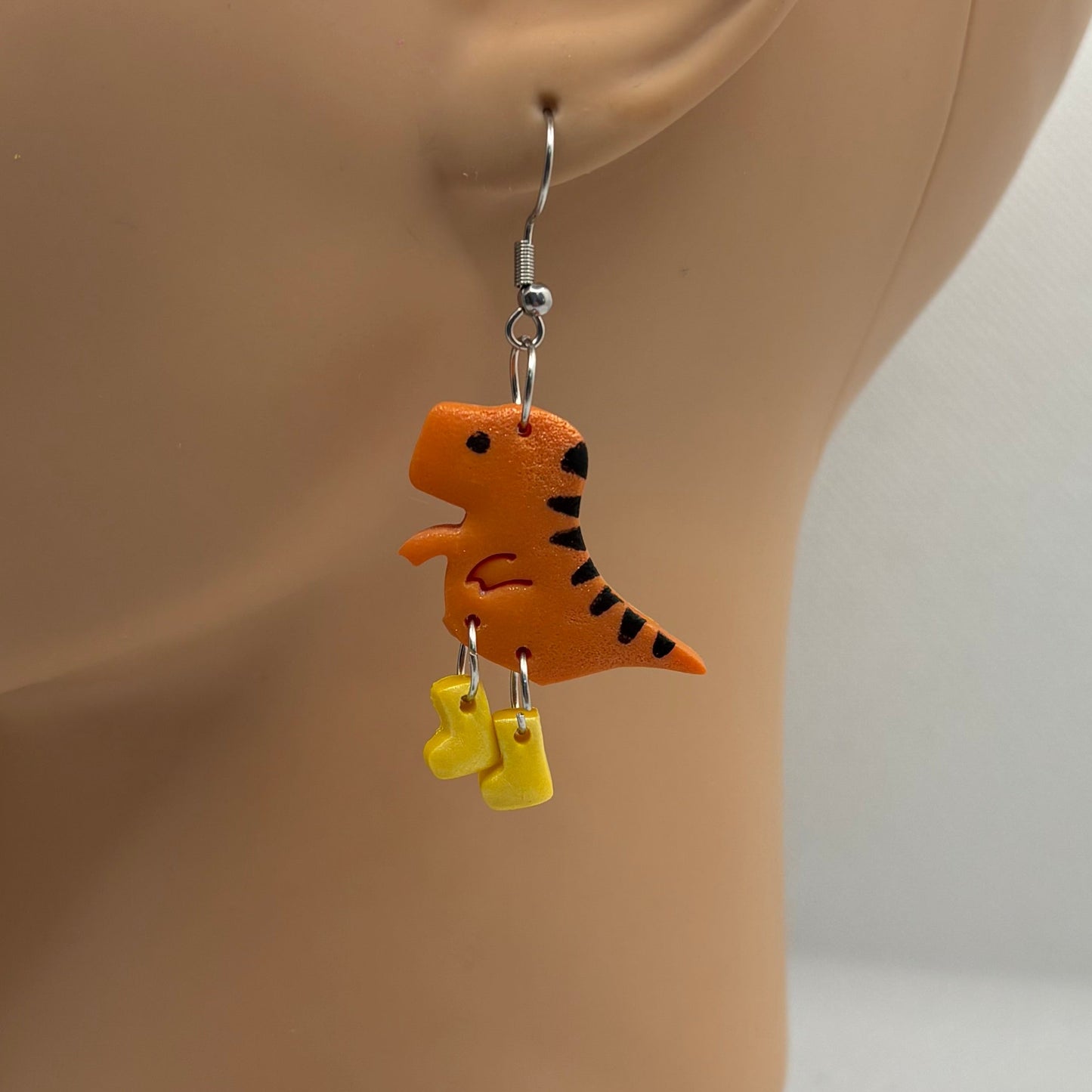 Dinosaur themed earrings with yellow gumboots hanging from the ear of a mannequin head.