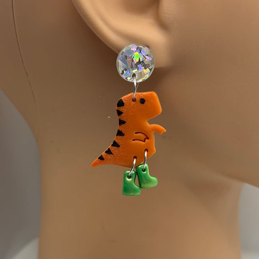 Dinosaur themed earrings with green gumboots hanging from the ear of a mannequin head.