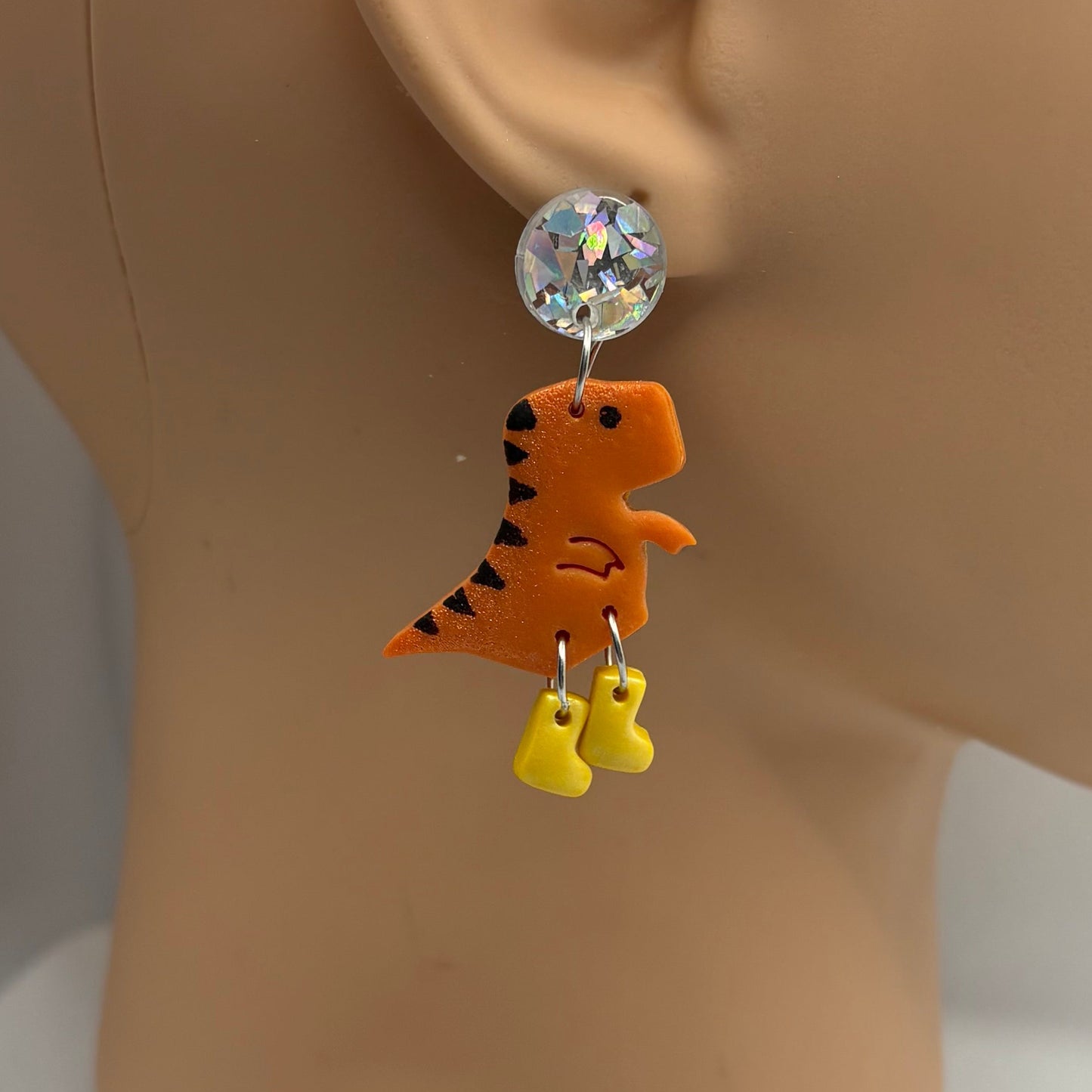 Dinosaur themed earrings with yellow gumboots hanging from the ear of a mannequin head.