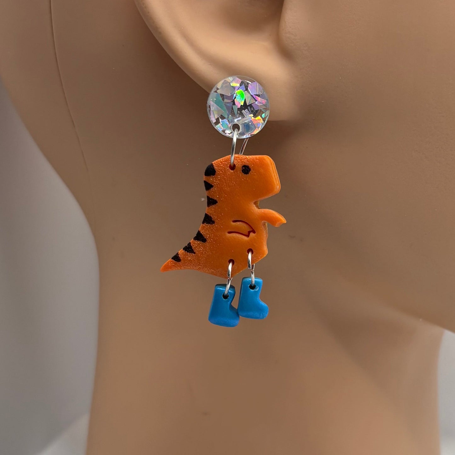 Dinosaur themed earrings with blue gumboots hanging from the ear of a mannequin head.