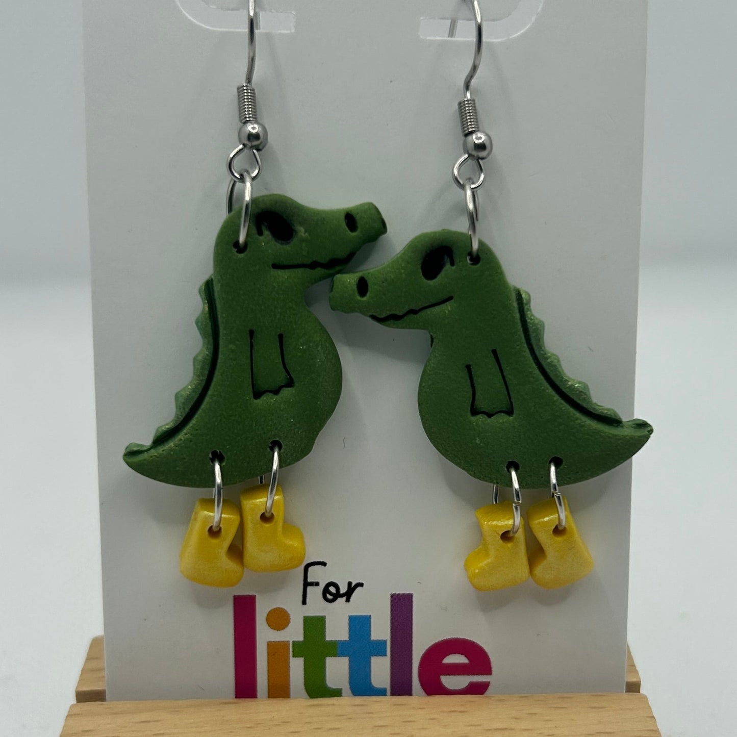 Green crocodile-shaped earrings with yellow gumboots on a display card.