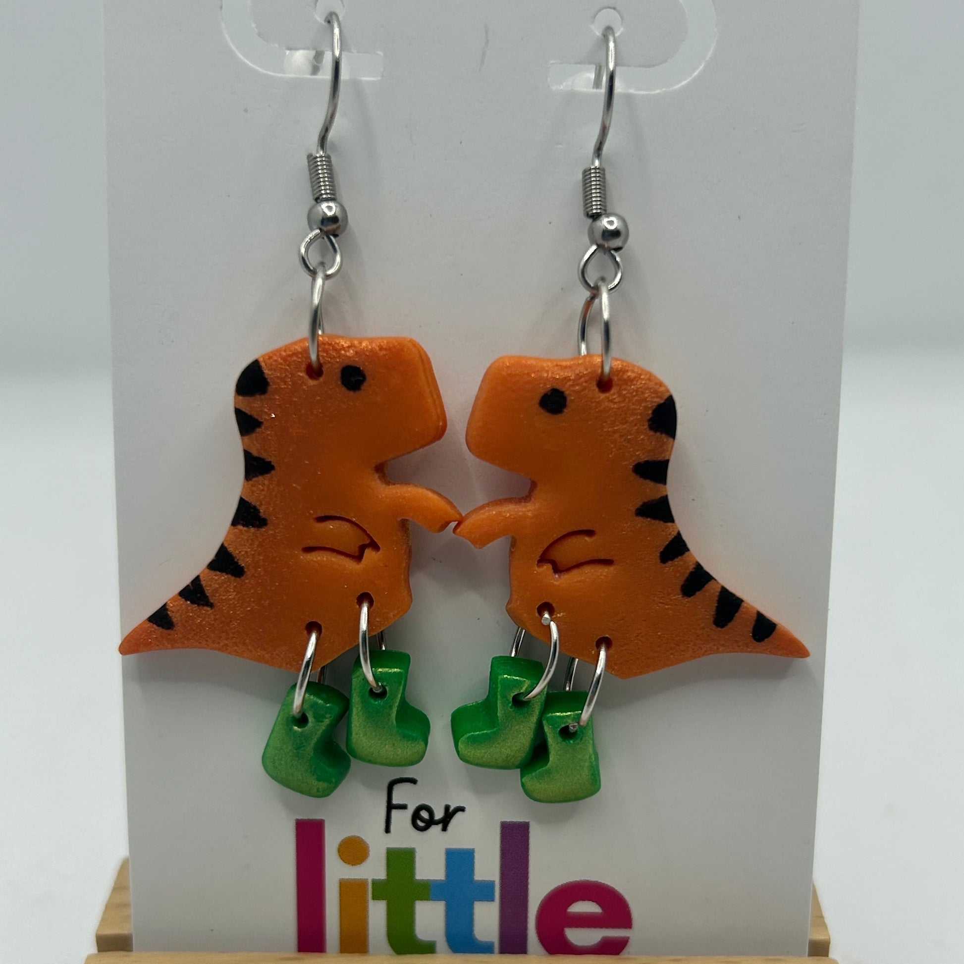 Dinosaur-shaped earrings with green gumboots on a display card.