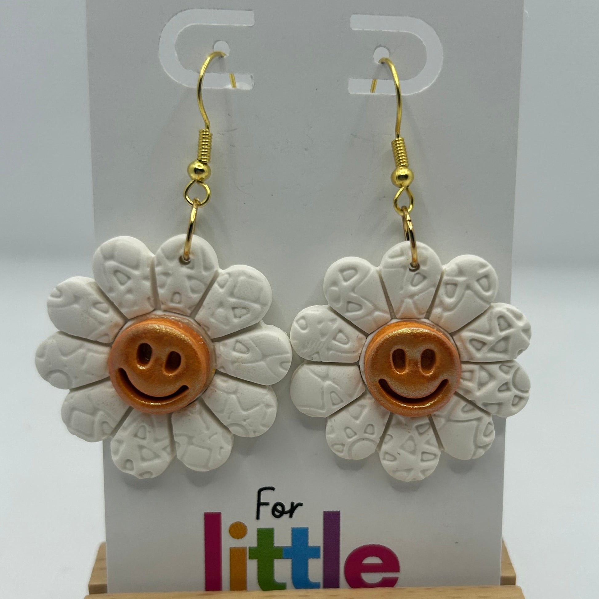 Flower-shaped earrings with smiley faces on a display card.