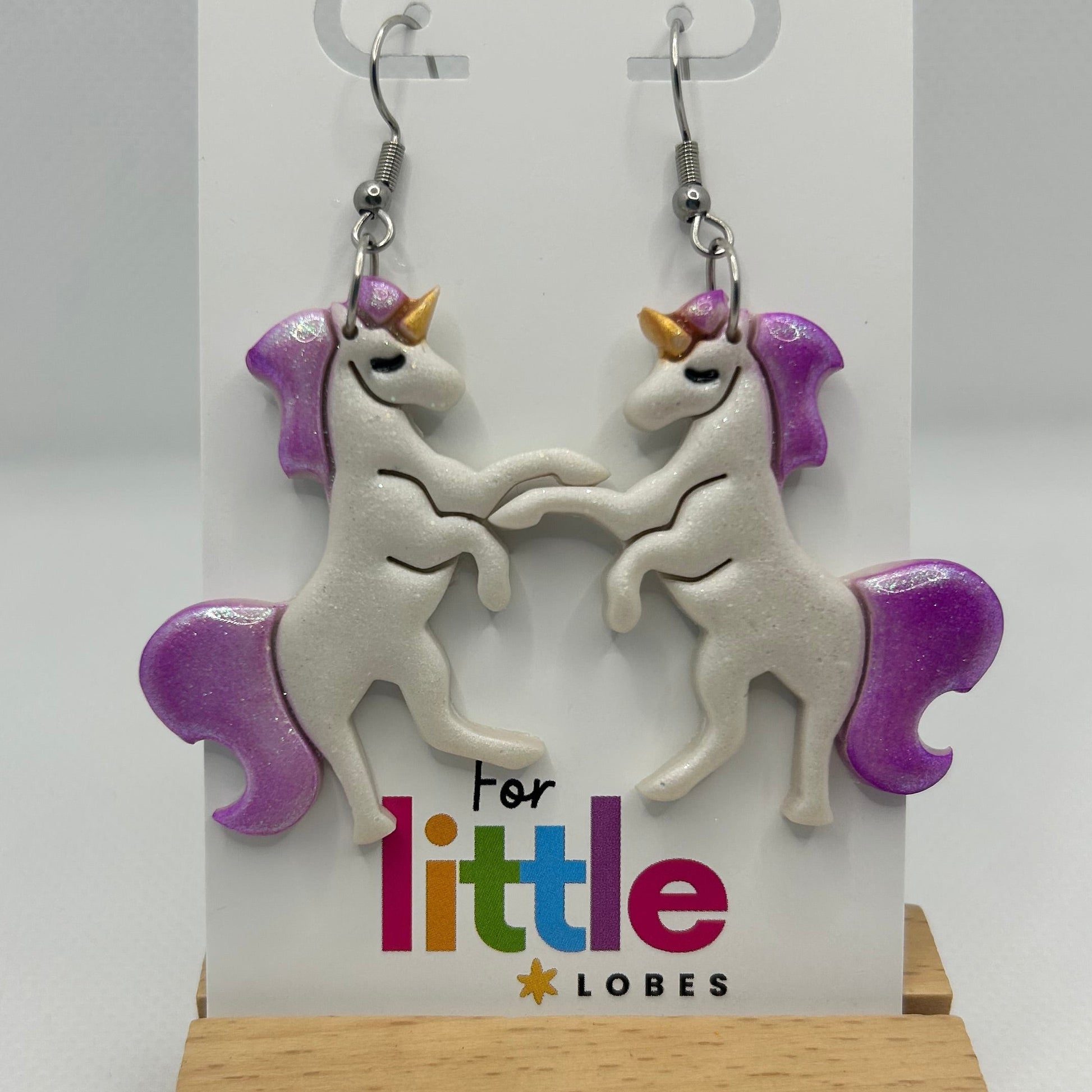 Unicorn-shaped earrings with purple manes and tails on a card with 'For little lobes' text