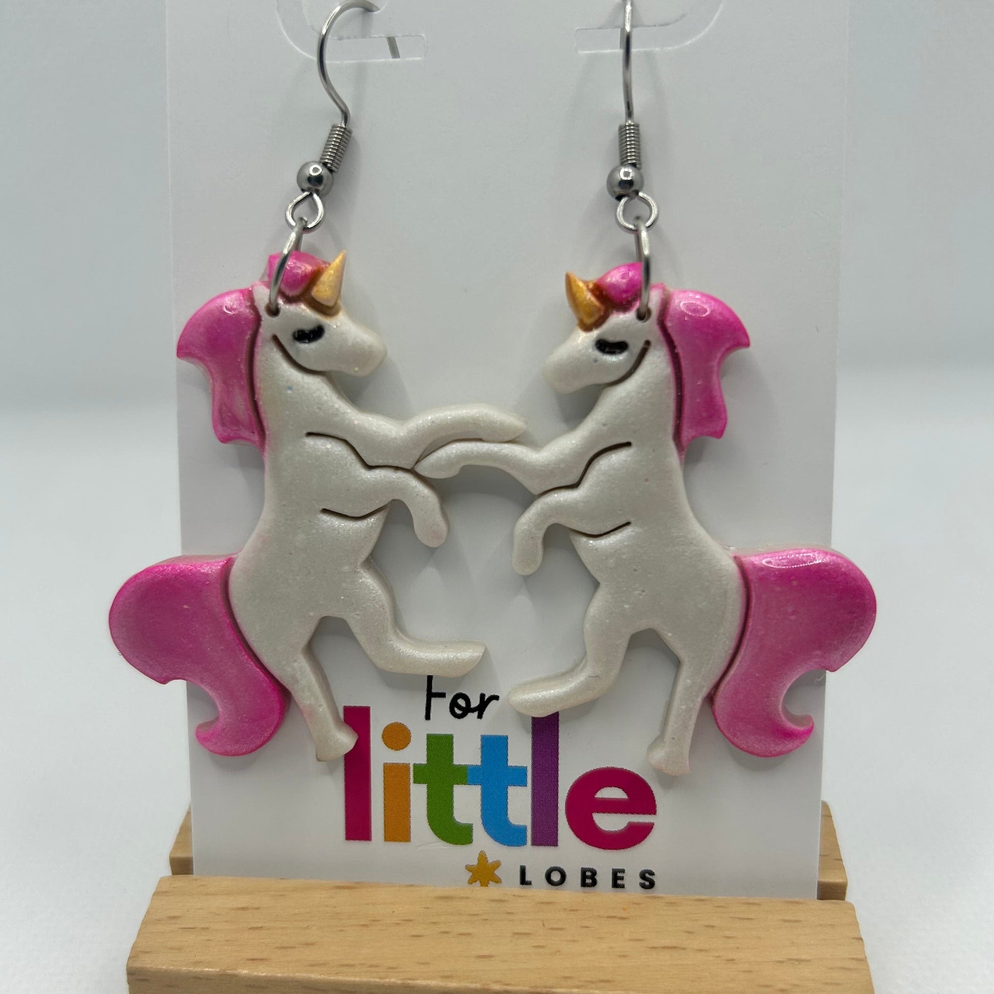 Unicorn-shaped earrings with pink manes and tails on a card with 'For little lobes' text