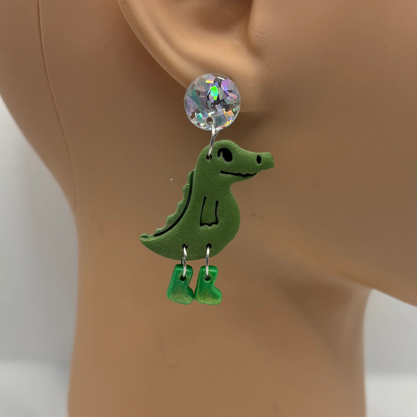 Green crocodile-shaped earrings with green gumboots on a mannequin head.