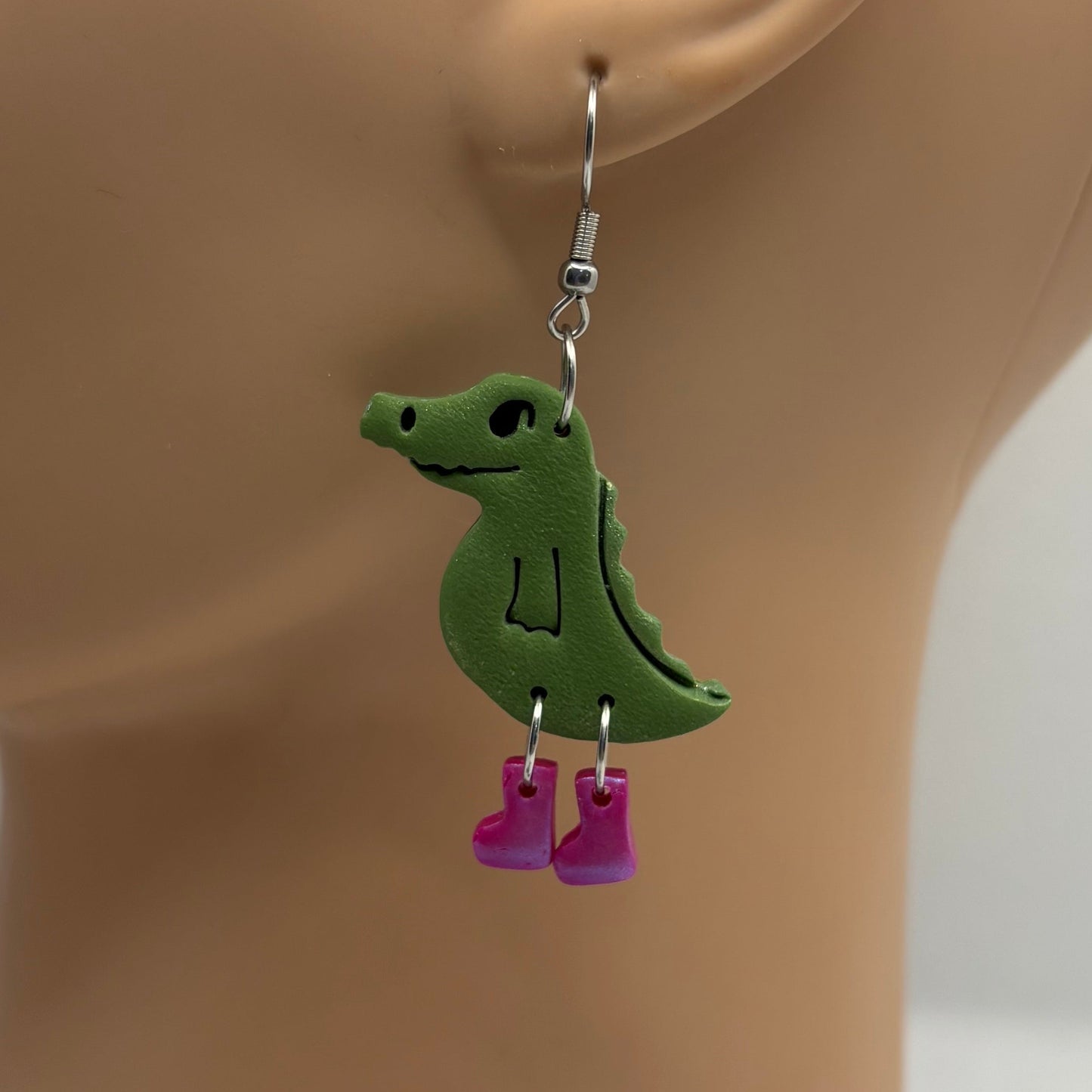 Green crocodile-shaped earrings with purple gumboots on a mannequin head.