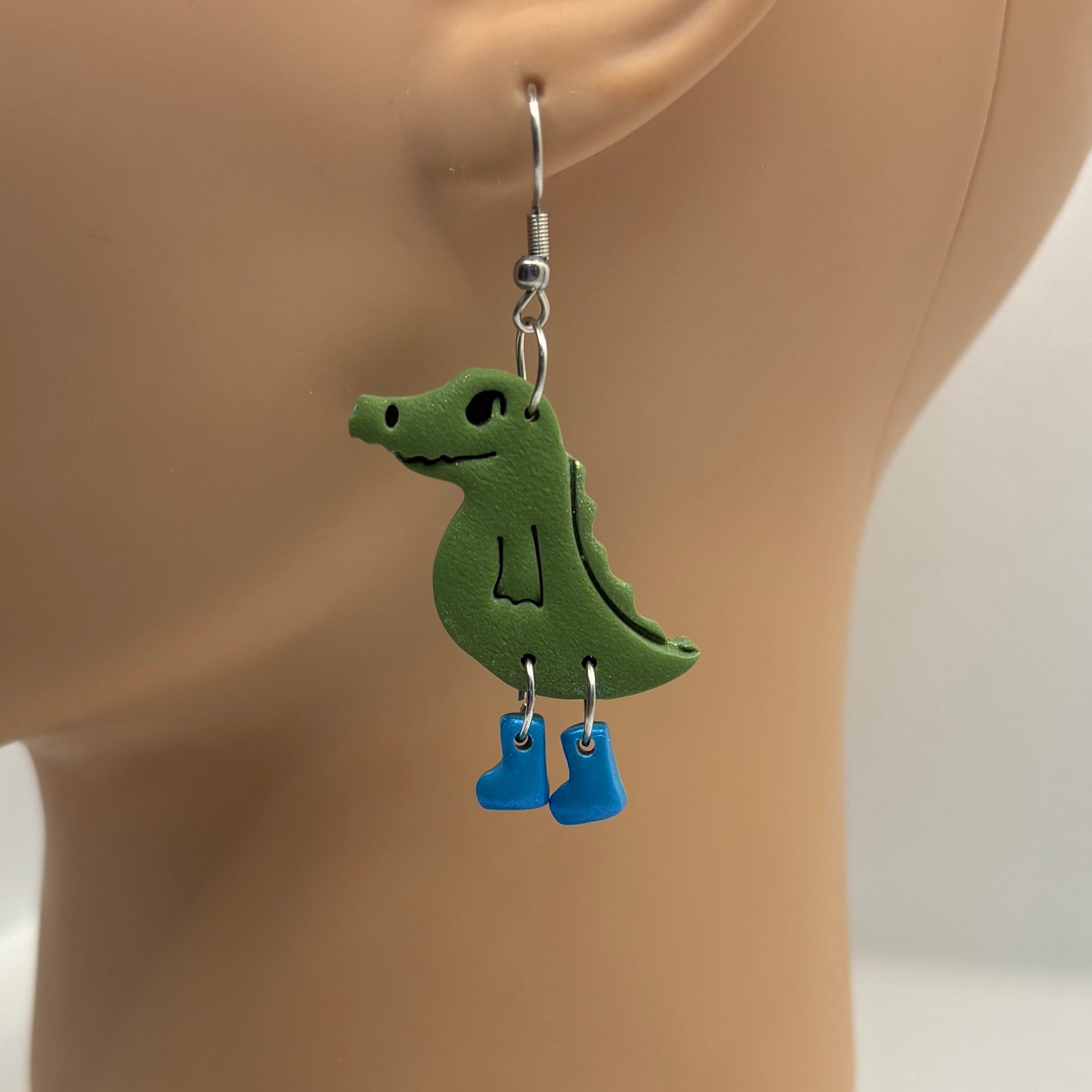 Green crocodile-shaped earrings with blue gumboots on a mannequin head.