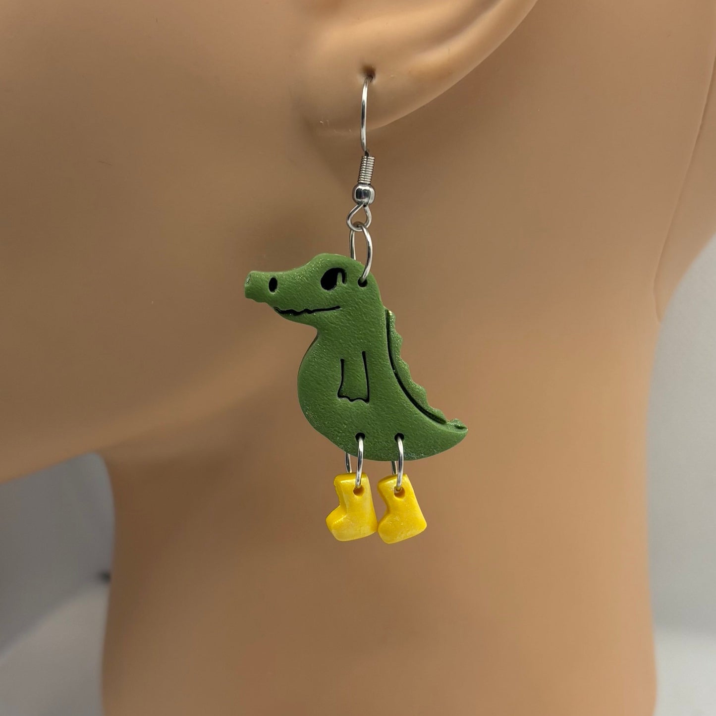 Green crocodile-shaped earrings with yellow gumboots on a mannequin head.