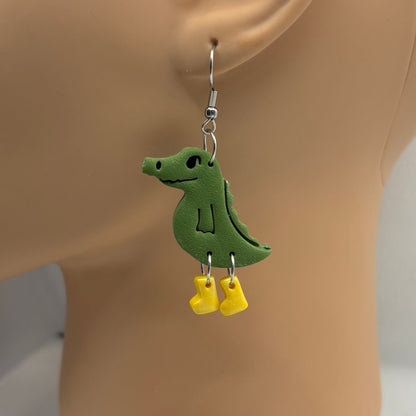 Green crocodile-shaped earrings with yellow gumboots on a mannequin head.