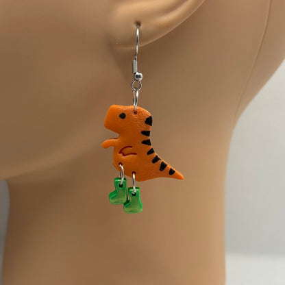 Dinosaur themed earrings with green gumboots hanging from the ear of a mannequin head.