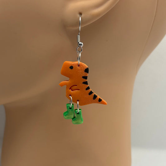 Dinosaur themed earrings with green gumboots hanging from the ear of a mannequin head.