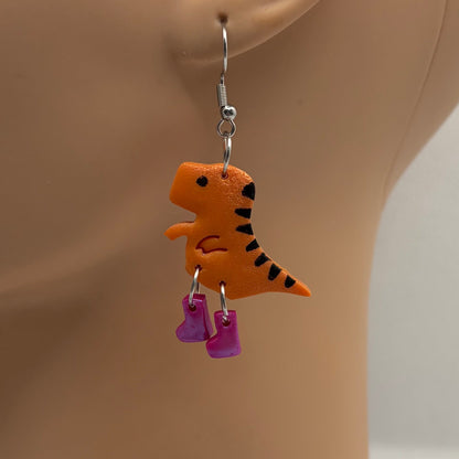 Dinosaur themed earrings with purple gumboots hanging from the ear of a mannequin head.