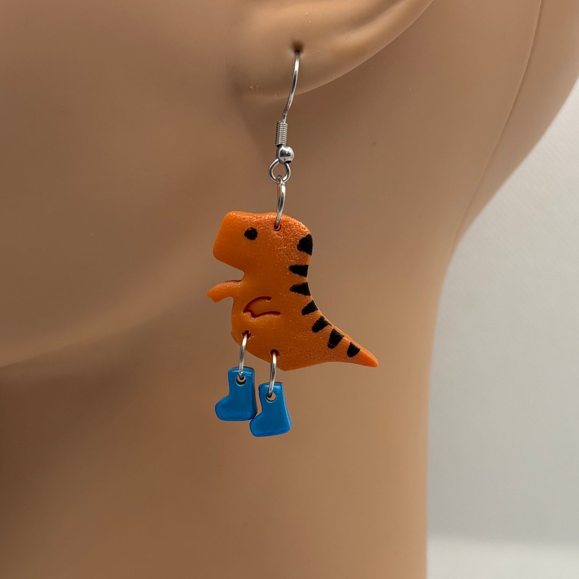 Dinosaur themed earrings with blue gumboots hanging from the ear of a mannequin head.