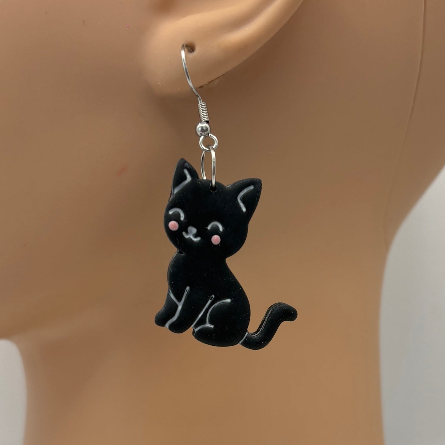 Black cat-shaped earring on a mannequin ear with a white background