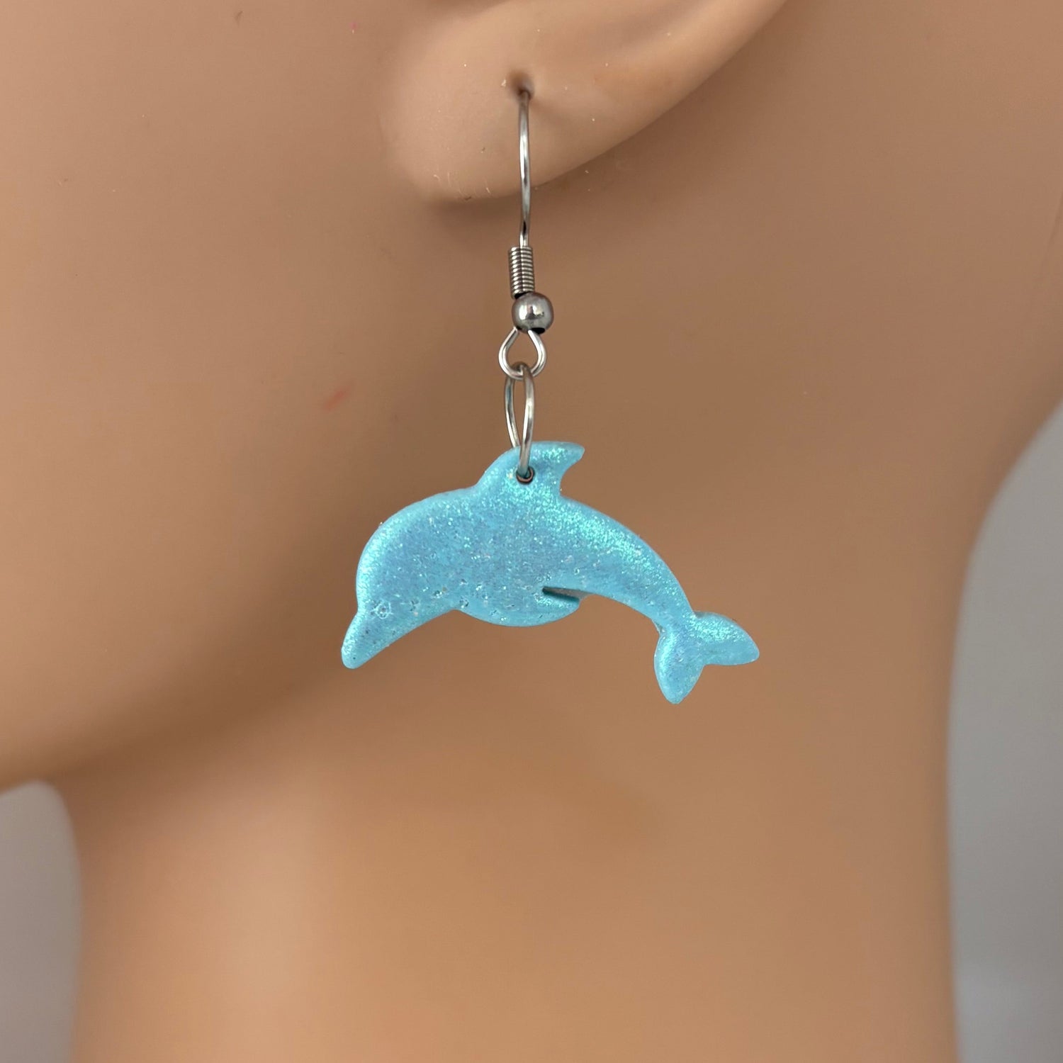 Blue dolphin-shaped earring on a mannequin ear